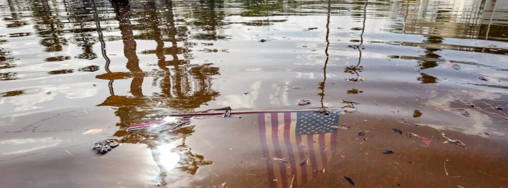 An American flag submerged in floodwaters after a hurricane in a residential neighborhood, symbolizing the aftermath of the storm.